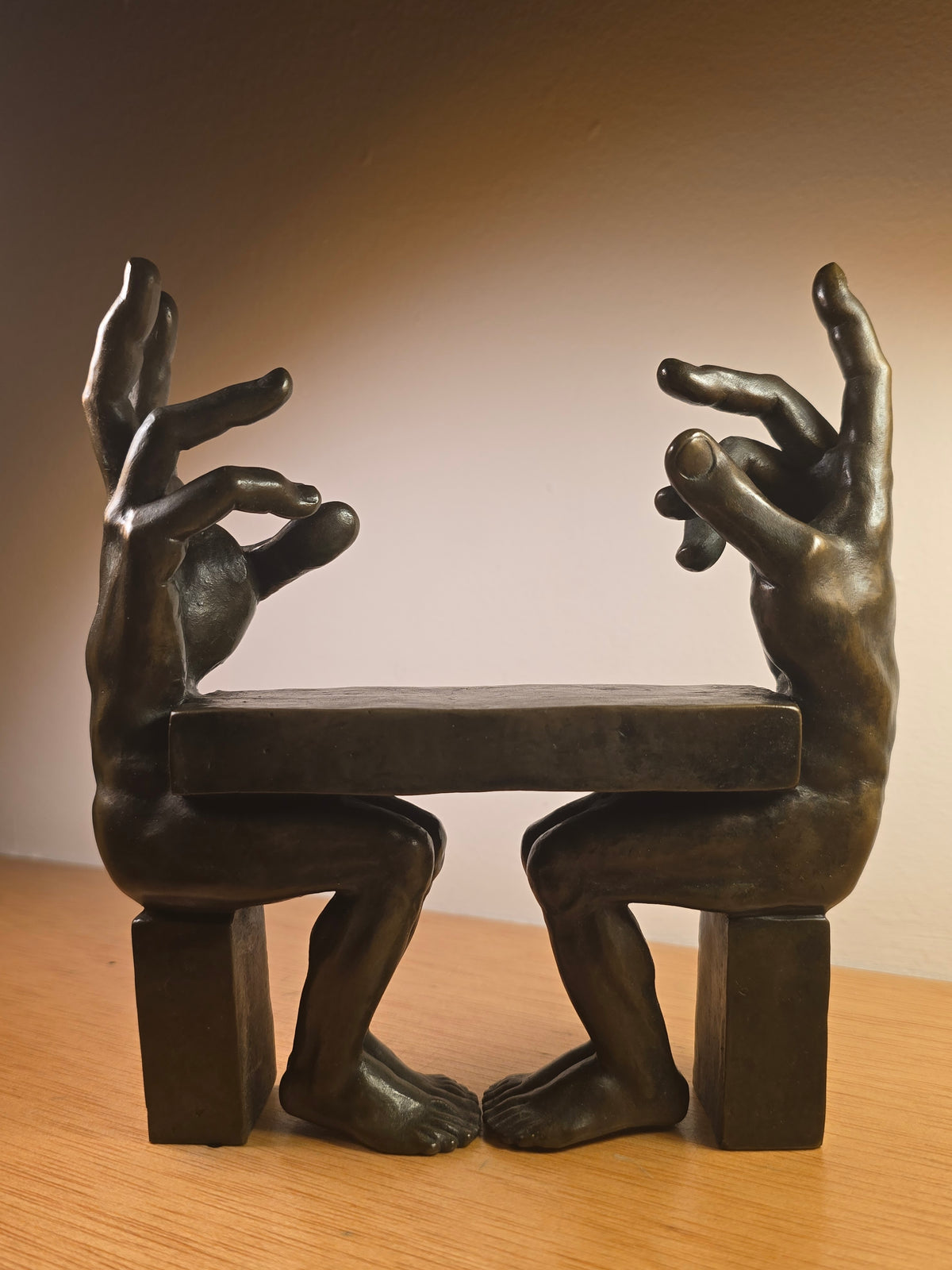 Bronze sculpture by German artist Michael Schwarze depicting two hand-like figures seated across a table. "Negotiation".