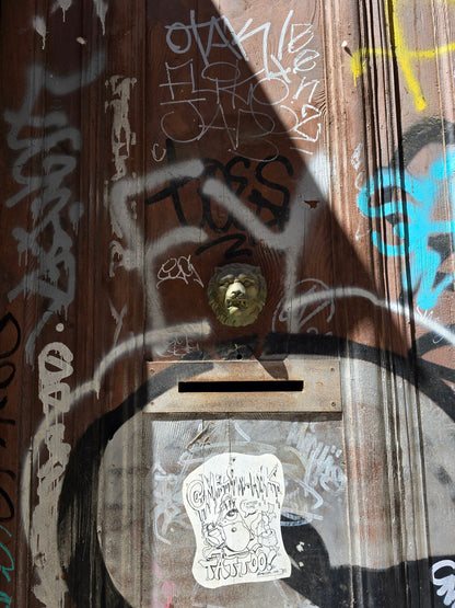 Weathered wooden mailbox covered in colorful graffiti and stickers on a Barcelona street.