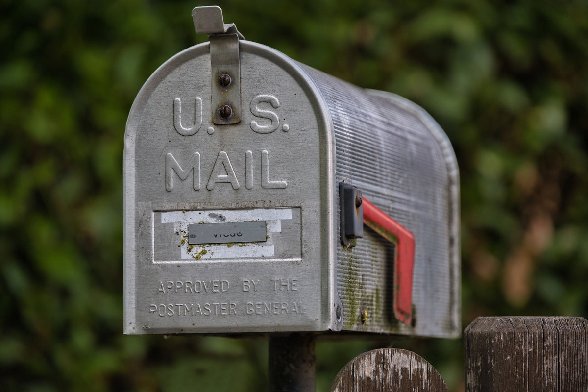 Gray U.S. mailbox with a red flag against a blurred green background